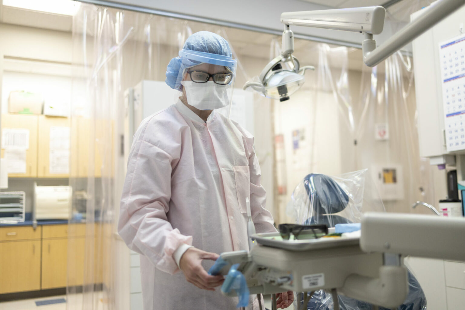 A dentist in full gown prepares her dental suite for an emergency, yet non-life-threatening, procedure.