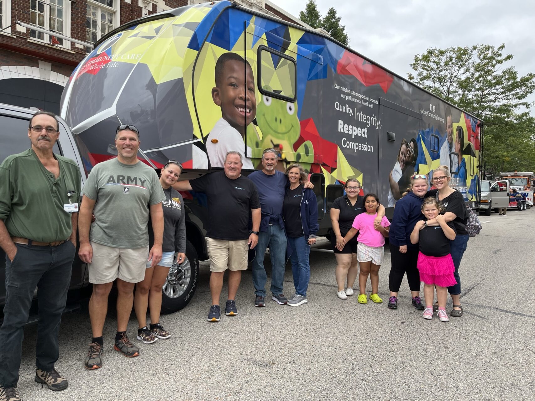 Families, doctors, and nurses stand in front of Hackley Community Care's mobile medical services unit in Muskegon, MI.